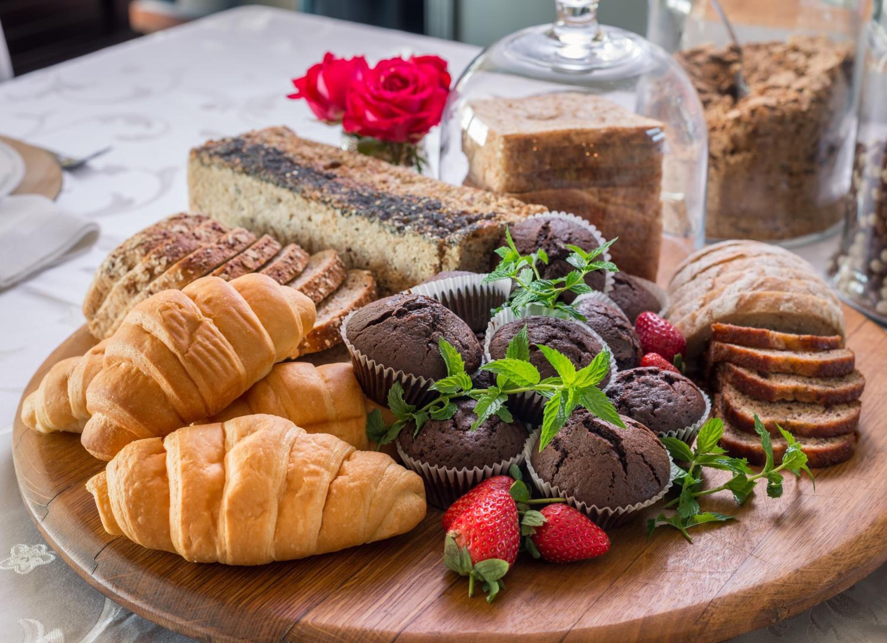 A variety of baked goods including croissants, muffins, and a cake on a wooden board.