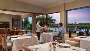 Un restaurante con mesas listas para comer, un camarero atendiendo a los clientes y una vista del lago al atardecer.