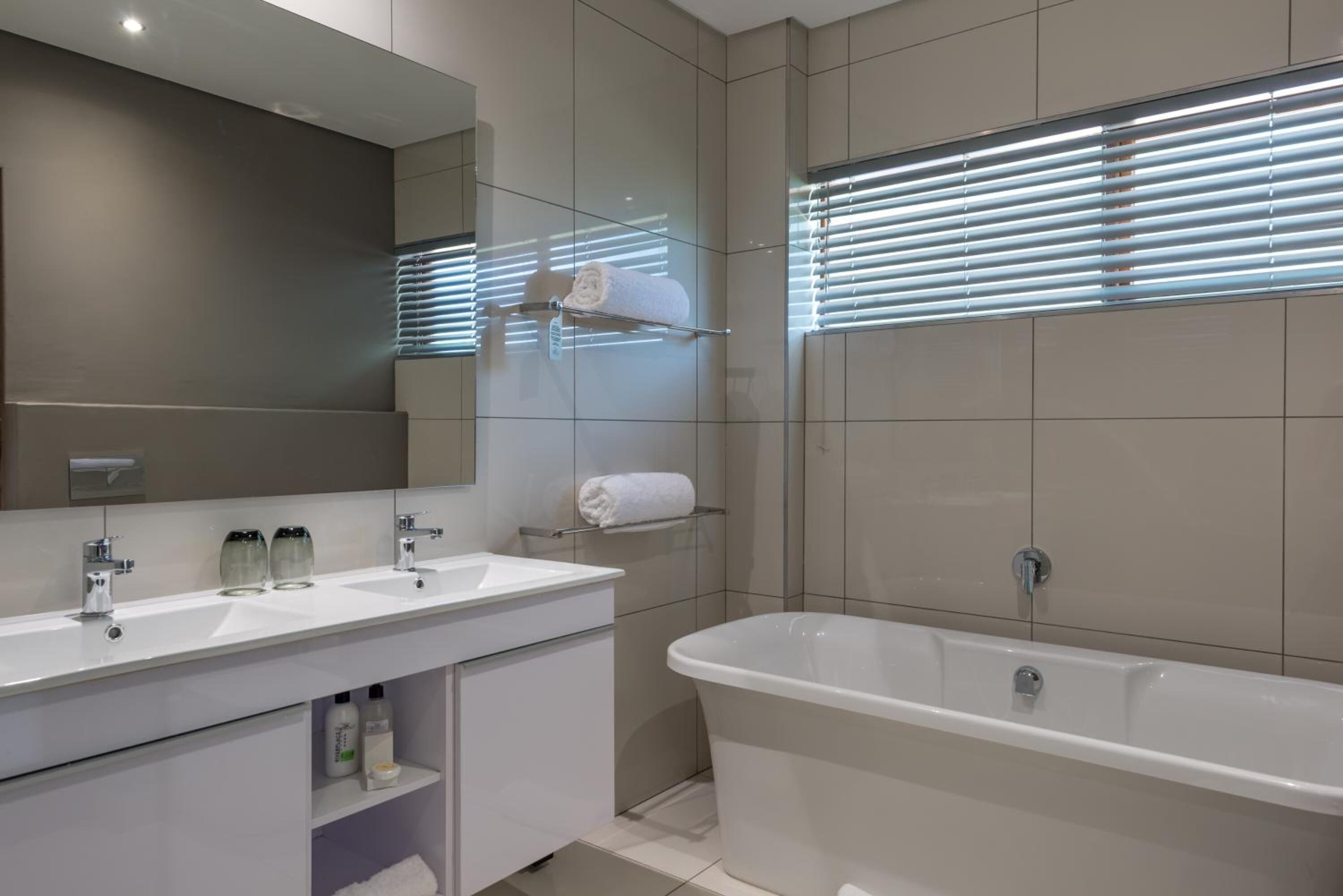 Un bany modern amb una banyera gran, dues dutxes i un mirall sobre el lavabo.