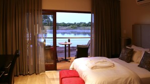 Habitación de hotel con cama, escritorio, una silla y vista a un lago a través de un ventanal.