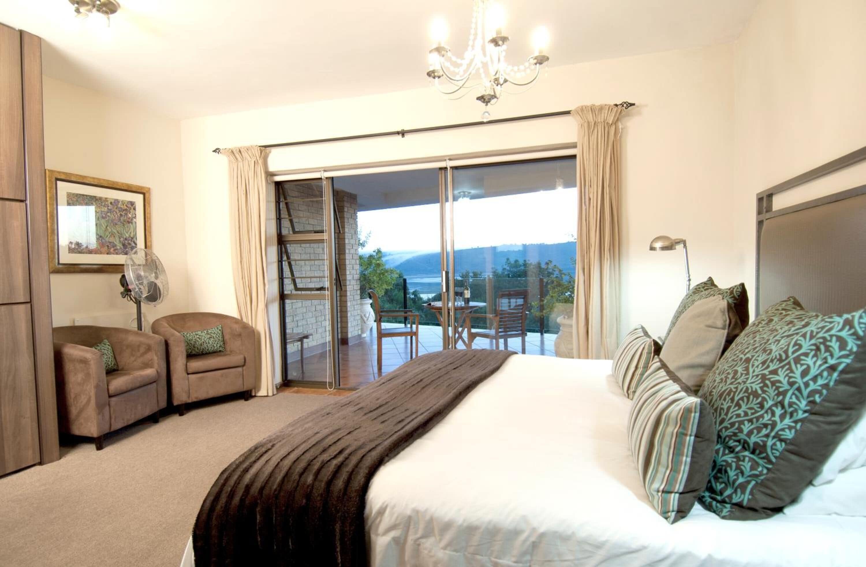 A bedroom with a large bed, a sliding glass door to a balcony, a chandelier, and a framed picture on the wall.