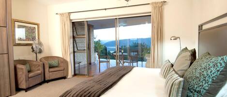 A bedroom with a large bed, a sliding glass door to a balcony, a chandelier, and a framed picture on the wall.