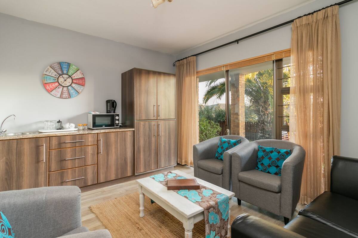 A compact living space with a kitchenette, a sofa set, a coffee table, and a large window with curtains.