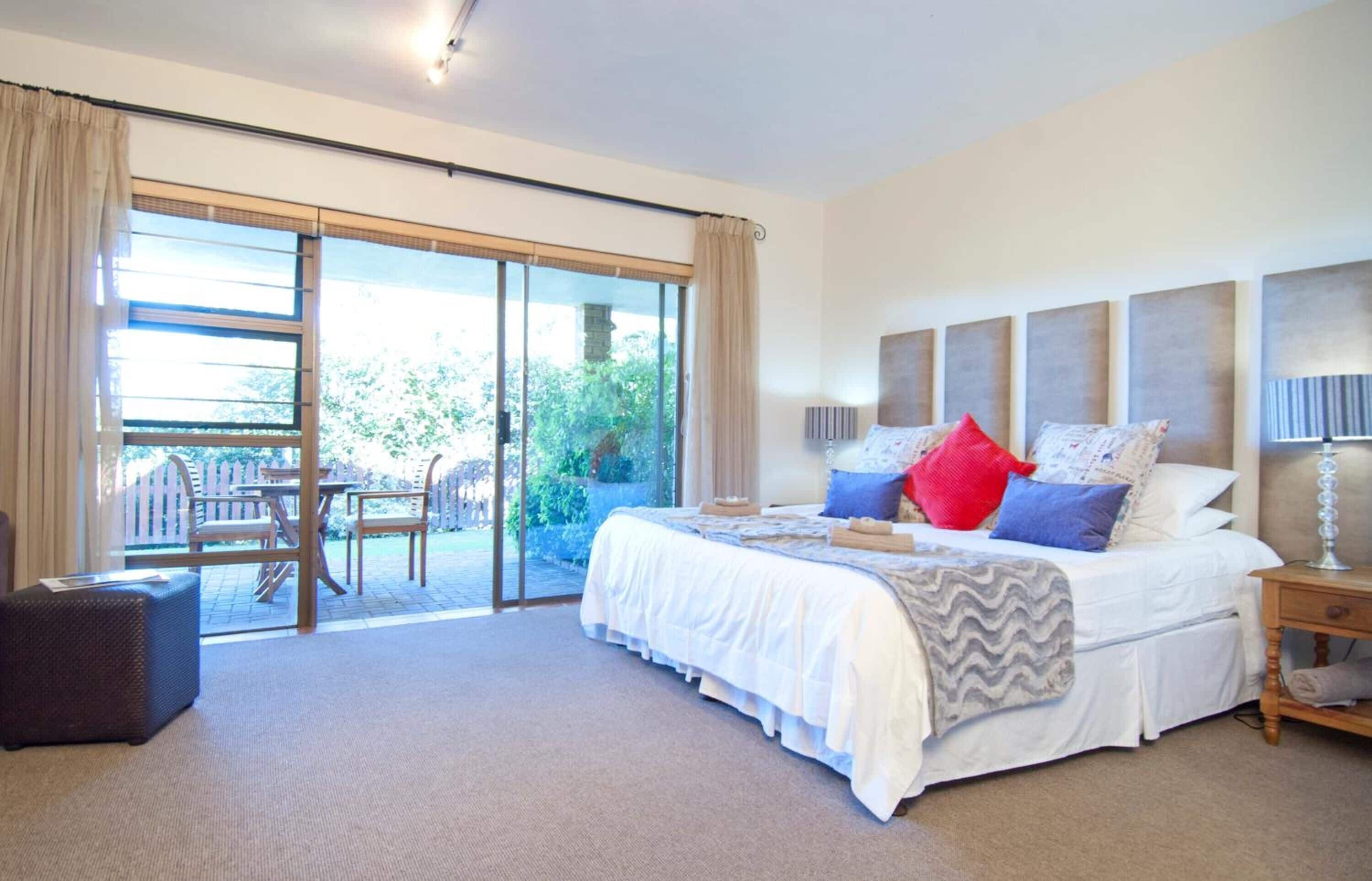 Un dormitorio con una cama grande, una mesita de noche, una lámpara, una silla y un ventanal corredera que da a un patio exterior.