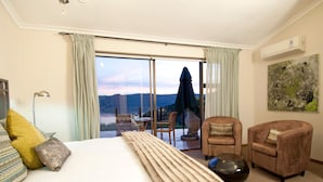 A hotel room with a large bed, two armchairs, a table, and a view of the outdoors. - Overmeer Guest House (Knysna)