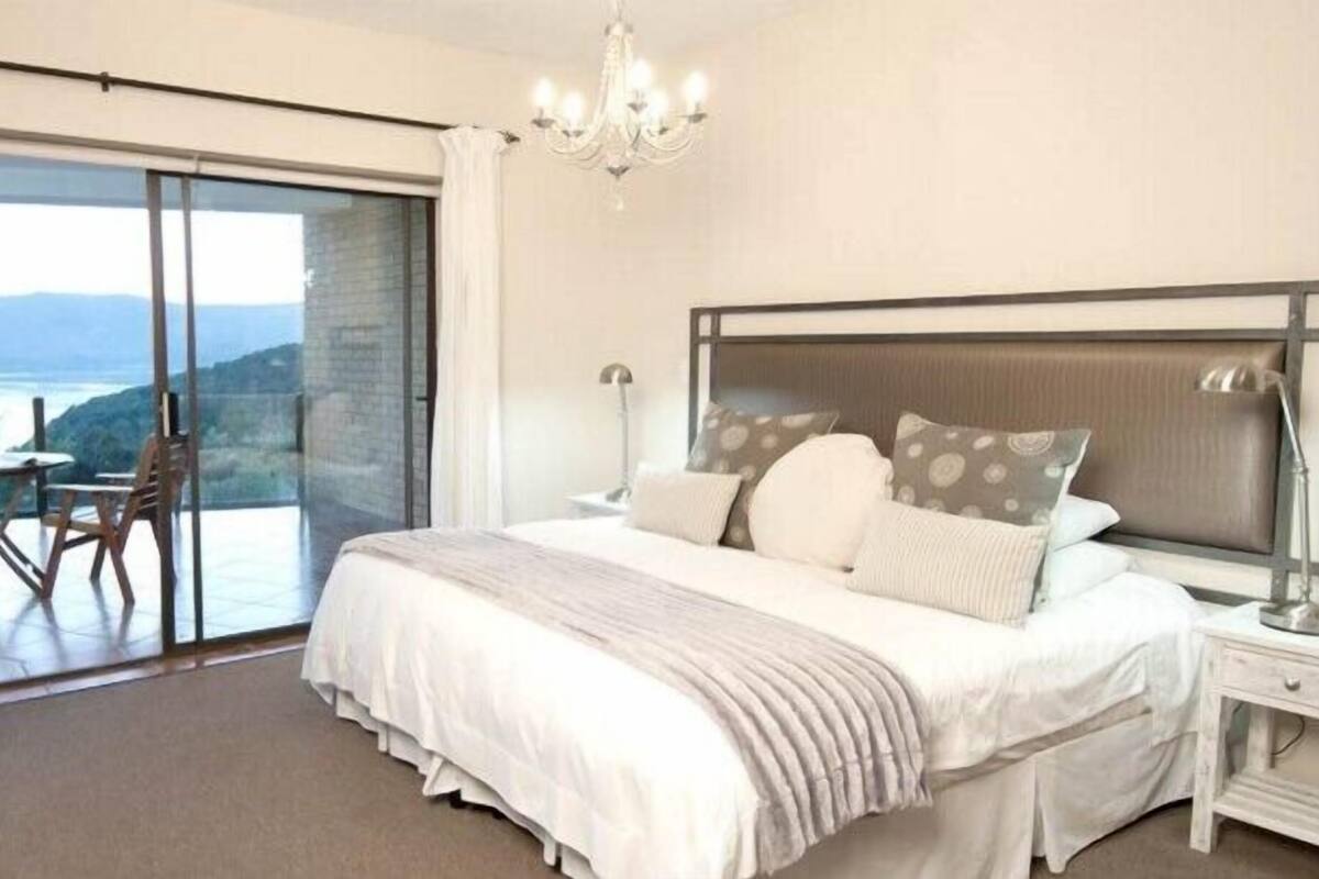 A bedroom with a large bed, a nightstand, a chair, and a view of the outdoors through a sliding door.