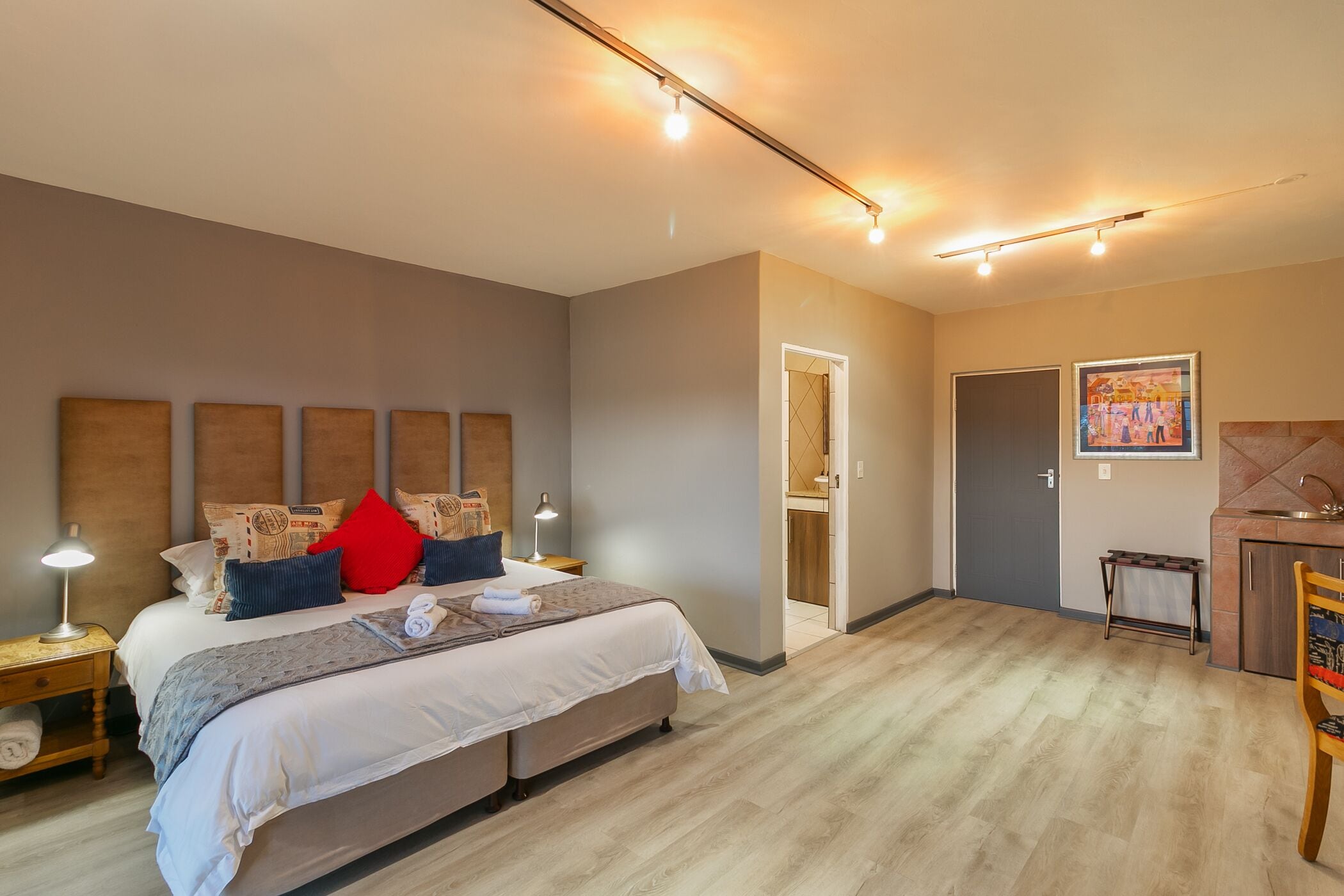 A bedroom with a large bed, bedside lamps, a small table, and a door leading to a bathroom.