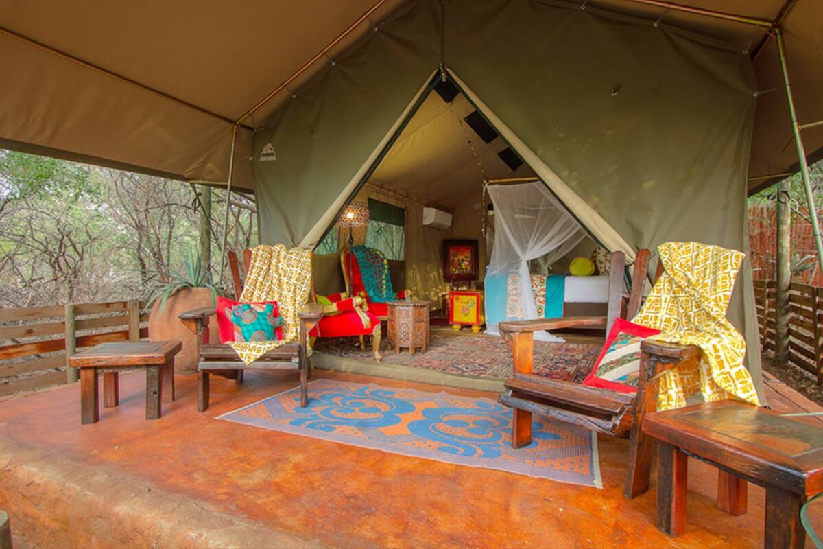 A tent with a wooden floor, a bed with a canopy, and a small table with chairs.