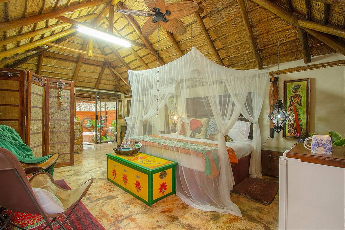 A room with a bed under a mosquito net, a wooden ceiling, a small table with a bowl, and a chair.