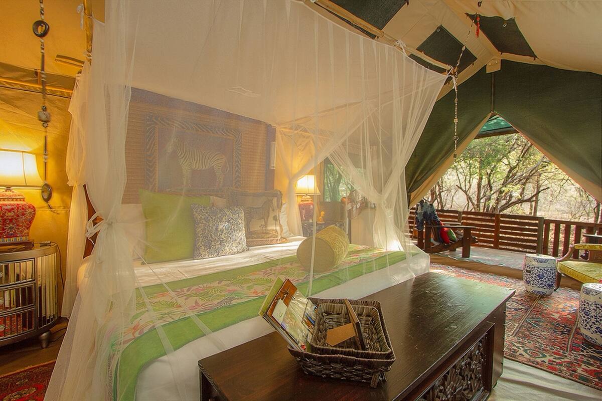 A room with a bed under a mosquito net, a wooden table, and a view of the outdoors.