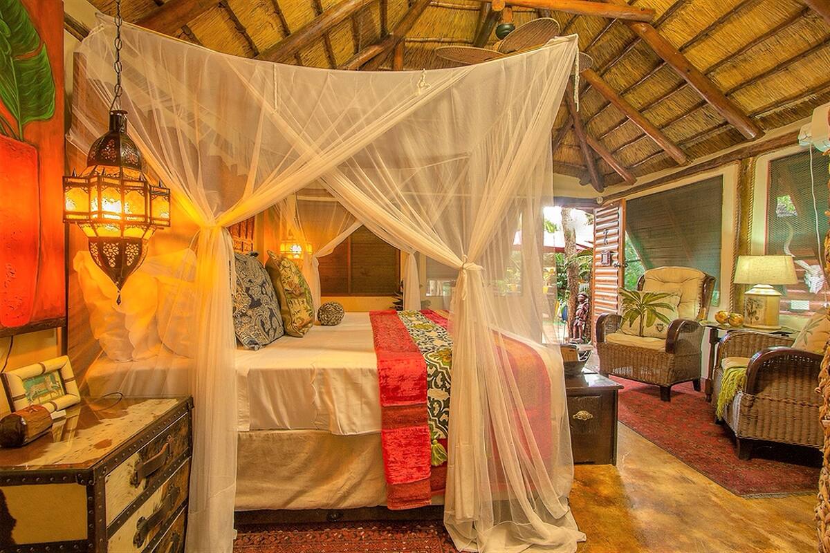 A room with a bed under a canopy, a nightstand, a lamp, and wicker furniture.