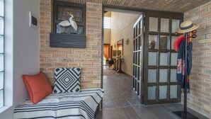 Une pièce chaleureuse avec un mur en briques, un banc agrémenté d’un coussin à motifs et une porte donnant sur un autre espace.