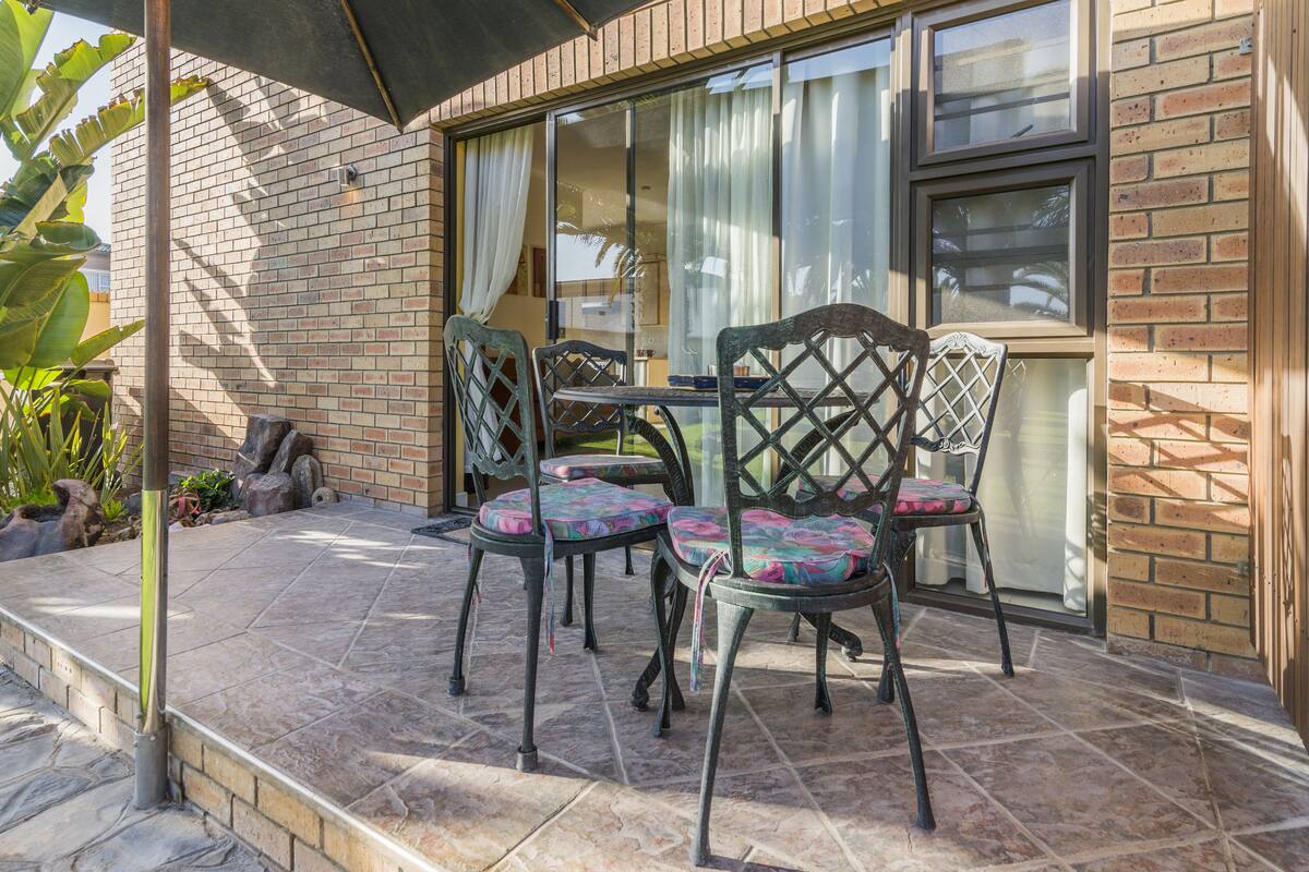 A patio with a table and chairs, a brick wall, and a window with curtains.