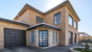 Une maison moderne à deux étages, avec une façade en briques, un garage et un jardin aménagé à l’avant.