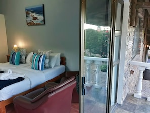 A hotel room with a bed, pillows, a painting, and a balcony with a stone wall and railing.