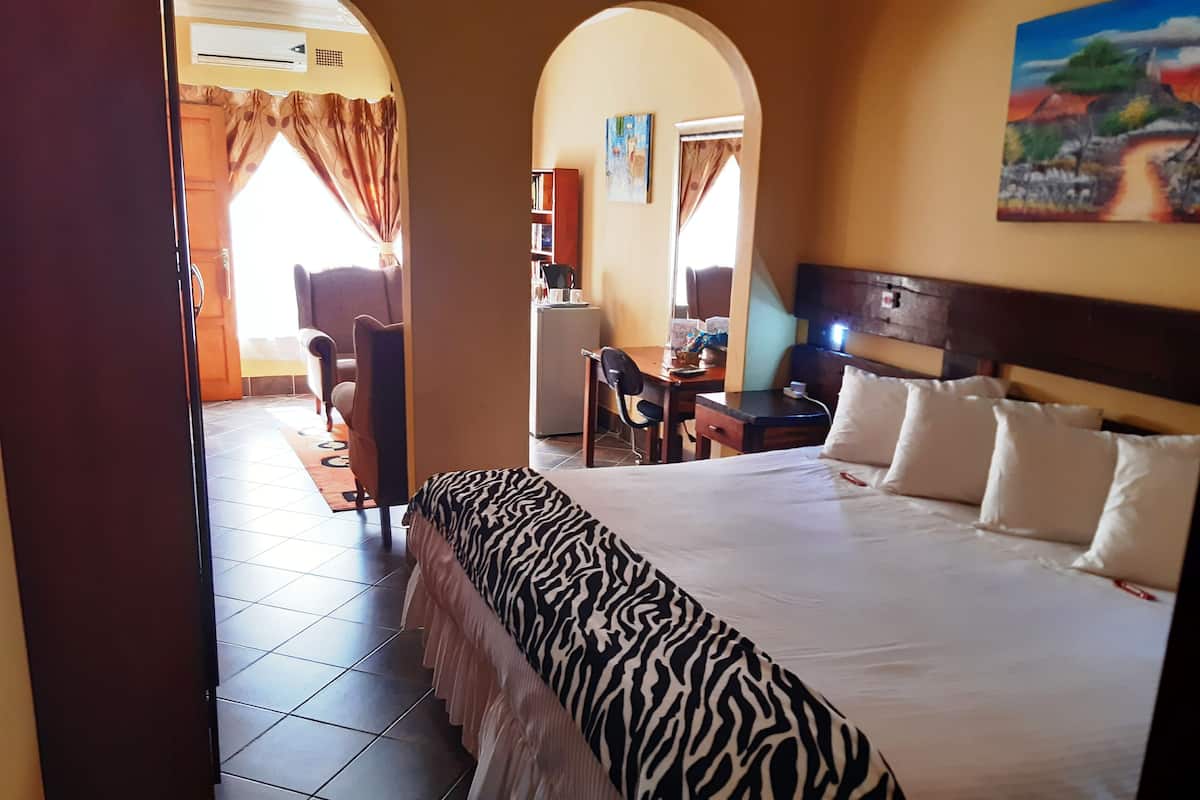 Une chambre d’hôtel avec un grand lit, un bureau et une chaise. Il y a un tableau au mur et une fenêtre avec des rideaux.