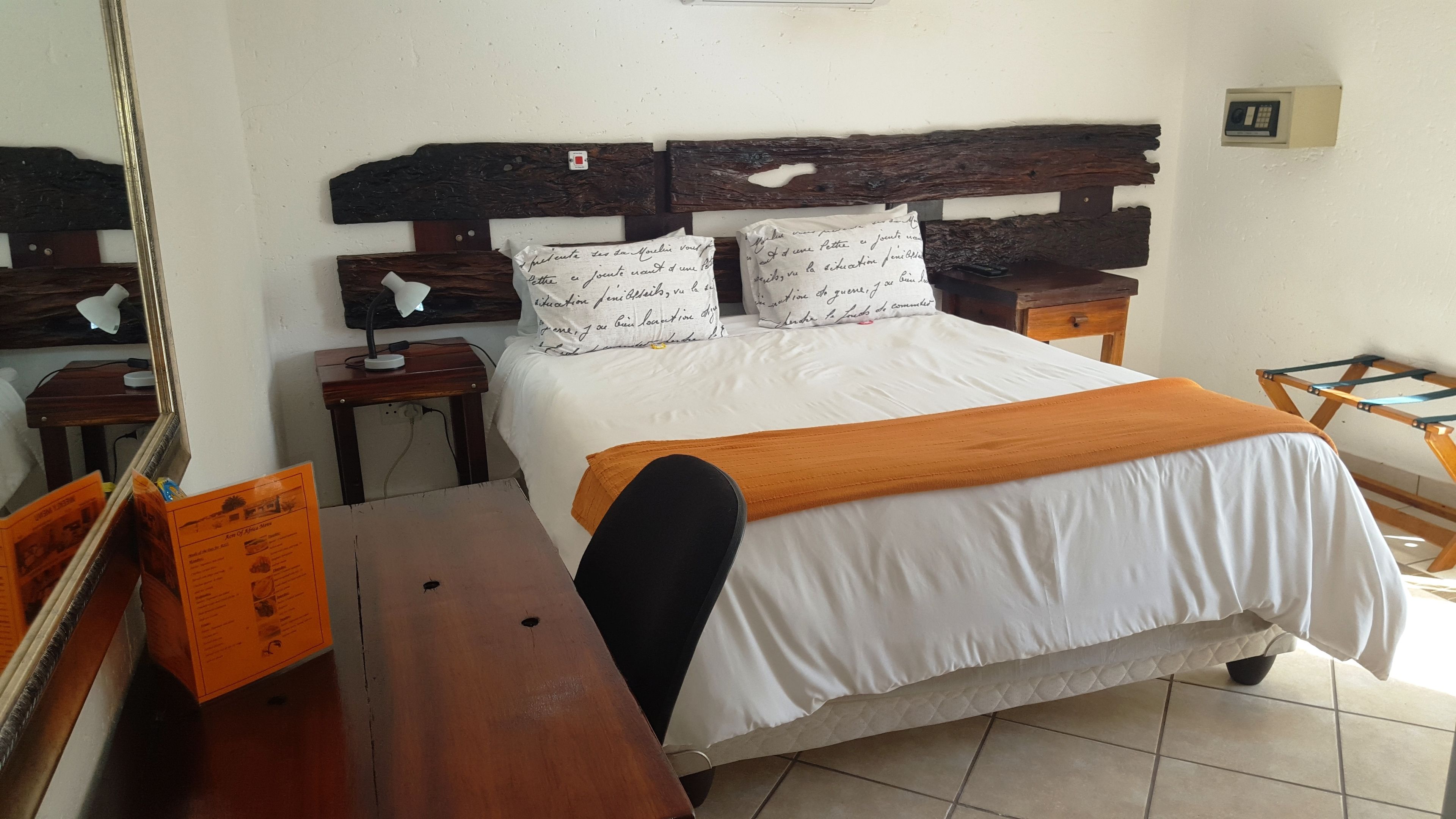 A bedroom with a wooden headboard, white bedding, a bedside table with a lamp, and a wooden bench.
