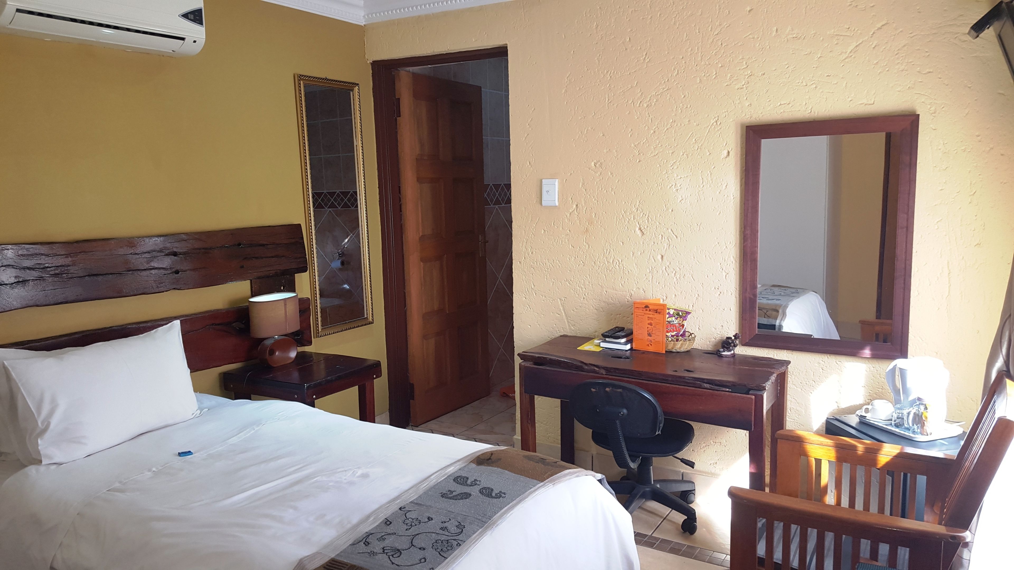 Una habitación de hotel con cama, escritorio, silla, espejo y puerta.