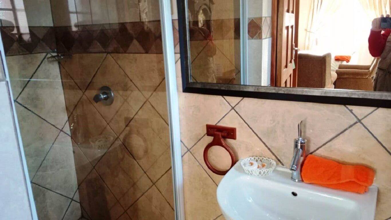 Un baño con mampara de vidrio, lavabo con jabonera y perchero.