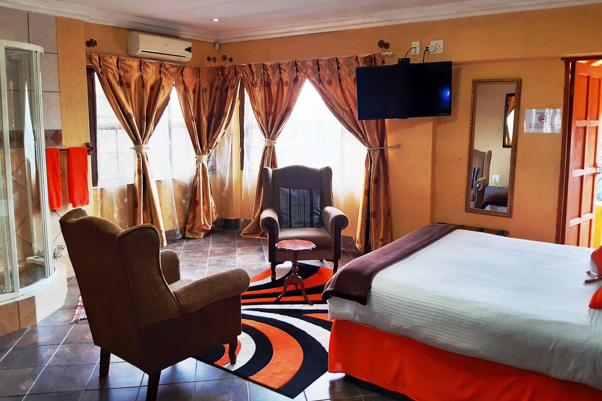 Une chambre d’hôtel avec un lit, une chaise, une télévision et une fenêtre avec des rideaux.