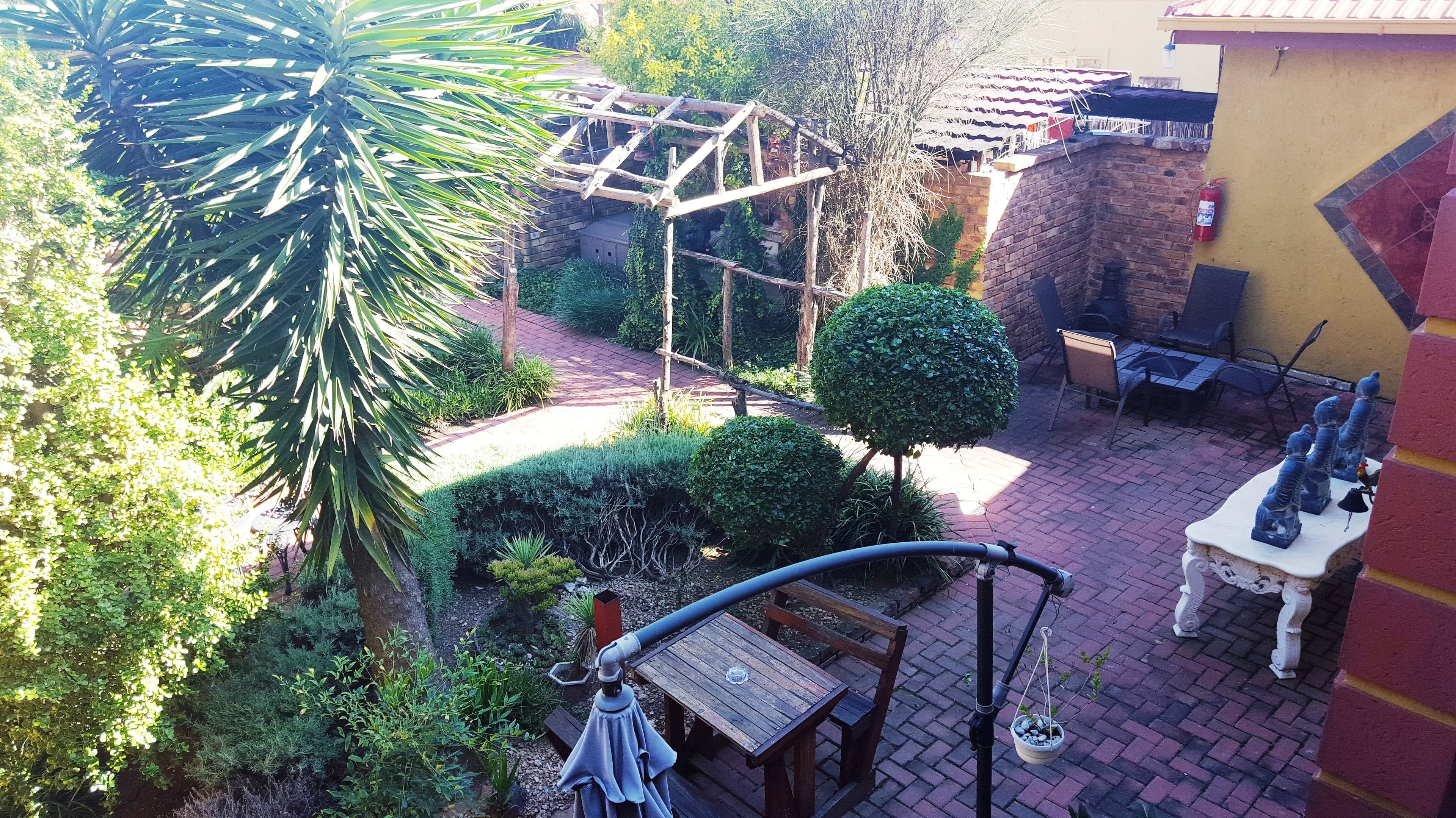 A patio area with a wooden table, chairs, and a small garden with various plants and a wooden trellis.