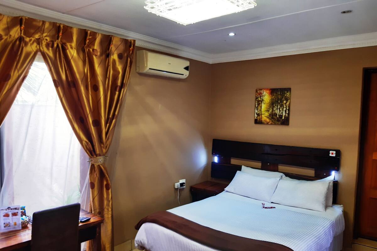 Une chambre d’hôtel avec un lit, un bureau, une chaise, un climatiseur et un tableau au mur.