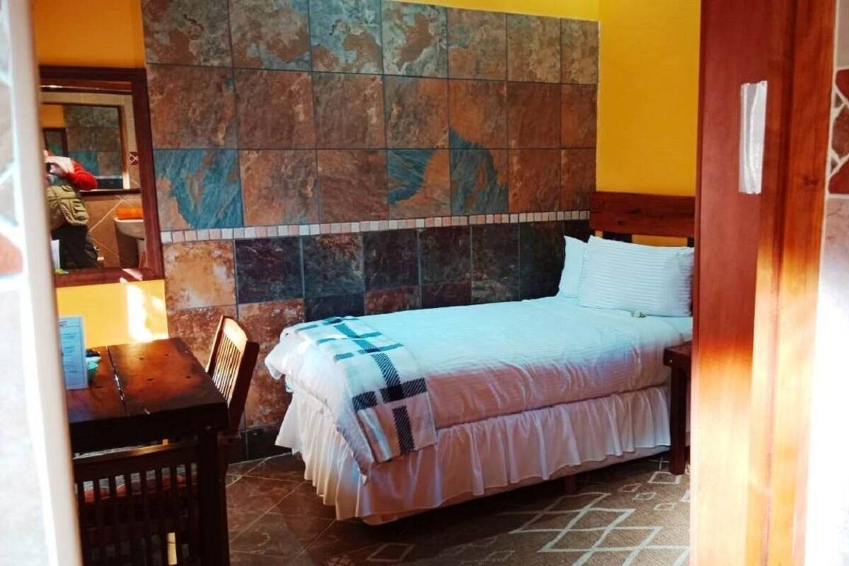 Une chambre à coucher avec un lit, une table de chevet en bois, un miroir et un mur recouvert de carreaux.