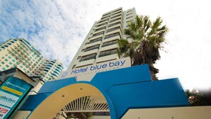 The entrance to Hotel Blue Bay with a clear view of the building's facade and a palm tree. - Blue Bay Hotel (Salinas)
