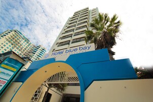 La entrada del Hotel Blue Bay, con vista despejada a la fachada del edificio y una palmera.