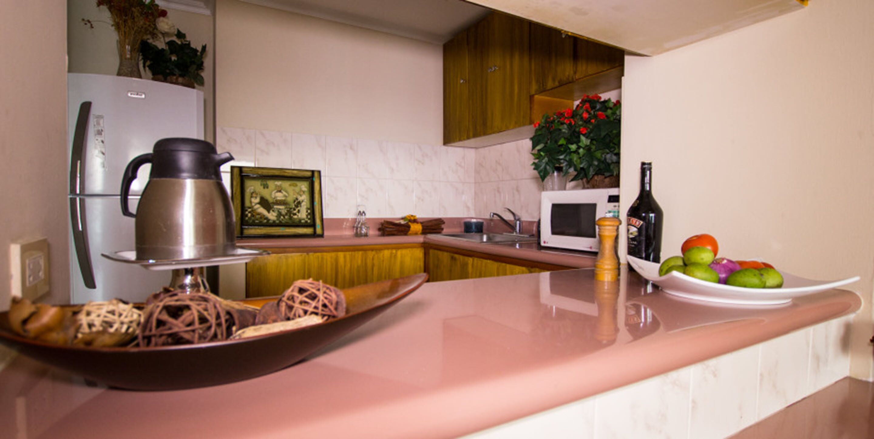 A kitchen with a refrigerator, microwave, and a fruit bowl on the counter.