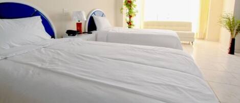 Habitación de hotel con dos camas, una mesita de noche con lámpara, teléfono y ventana con cortinas.