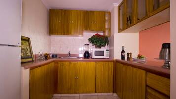 Una cocina con armarios de madera, microondas, lavabo y encimera con diversos objetos, incluyendo una planta y una botella.