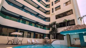 A multi-story hotel with a swimming pool, outdoor seating, and palm trees. - Blue Bay Hotel (Salinas)