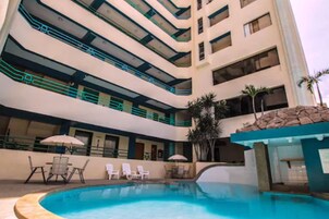 Un hotel de varios pisos con piscina, mobiliario exterior y palmeras.