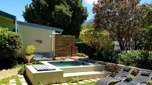 Zona de piscina exterior moderna amb gandules, una petita cascada i un mur de pedra.