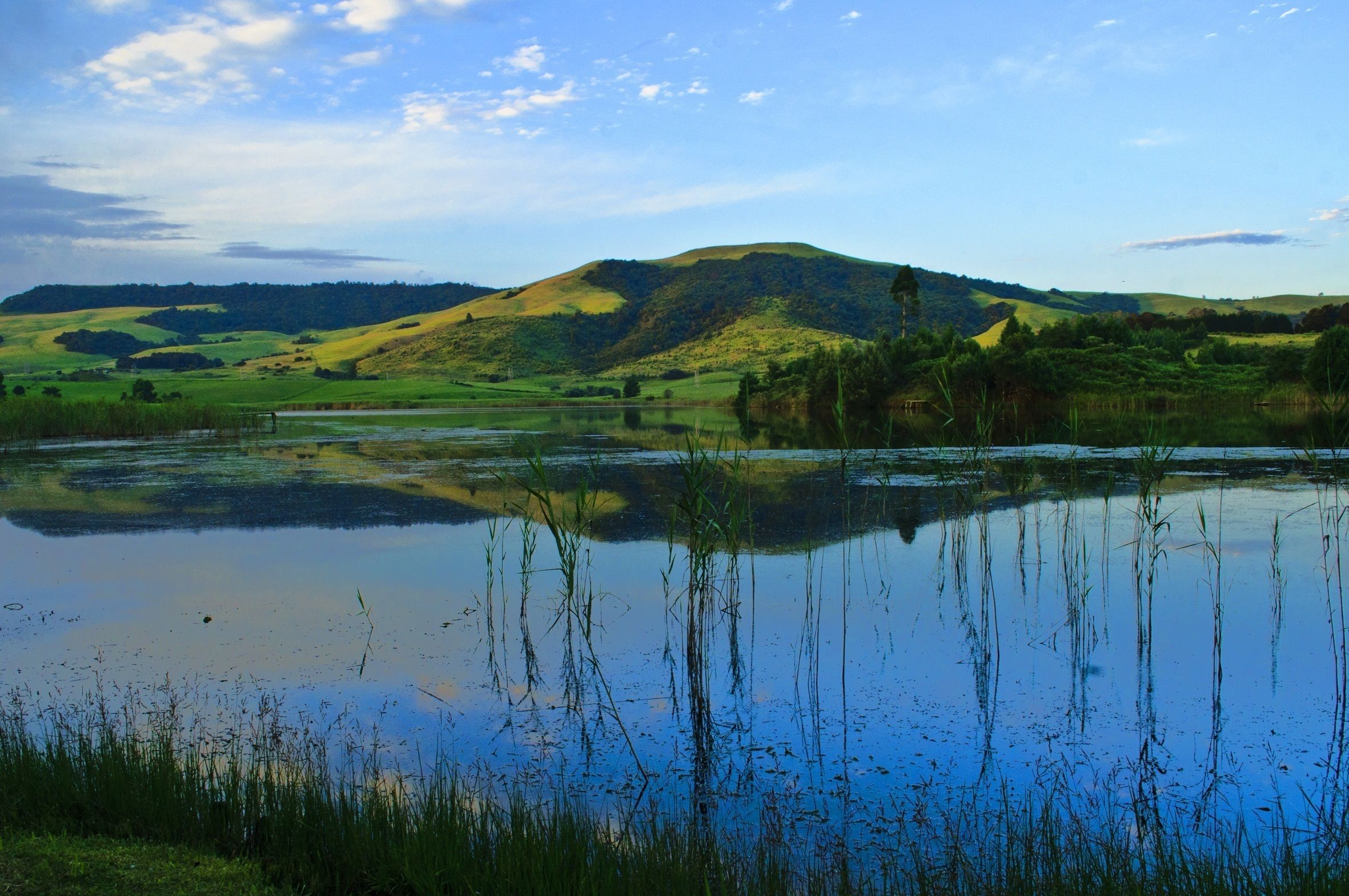 A serene landscape with a lake reflecting the sky and surrounding hills.