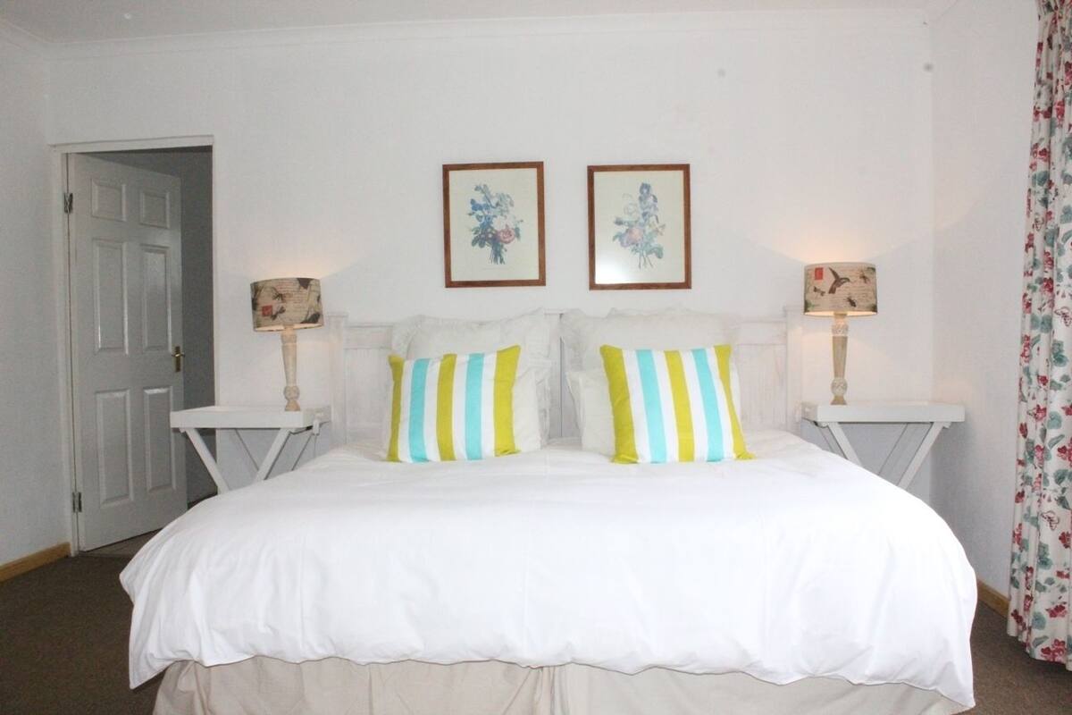 A bedroom with a large bed, two bedside tables with lamps, and two framed pictures on the wall.