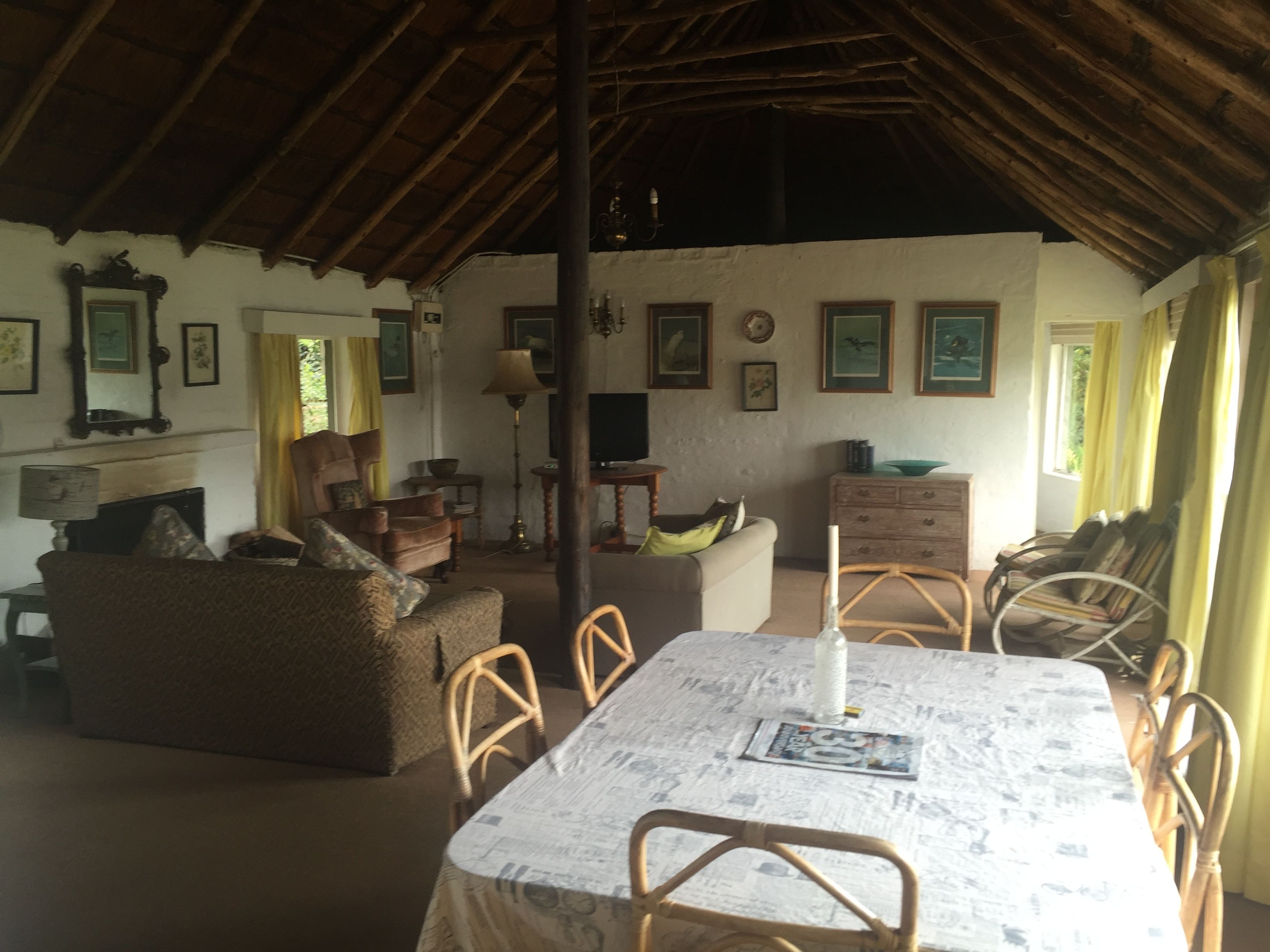 Uma sala de estar acolhedora com teto alto, mobiliário de madeira e uma mesa de jantar coberta com jornais.