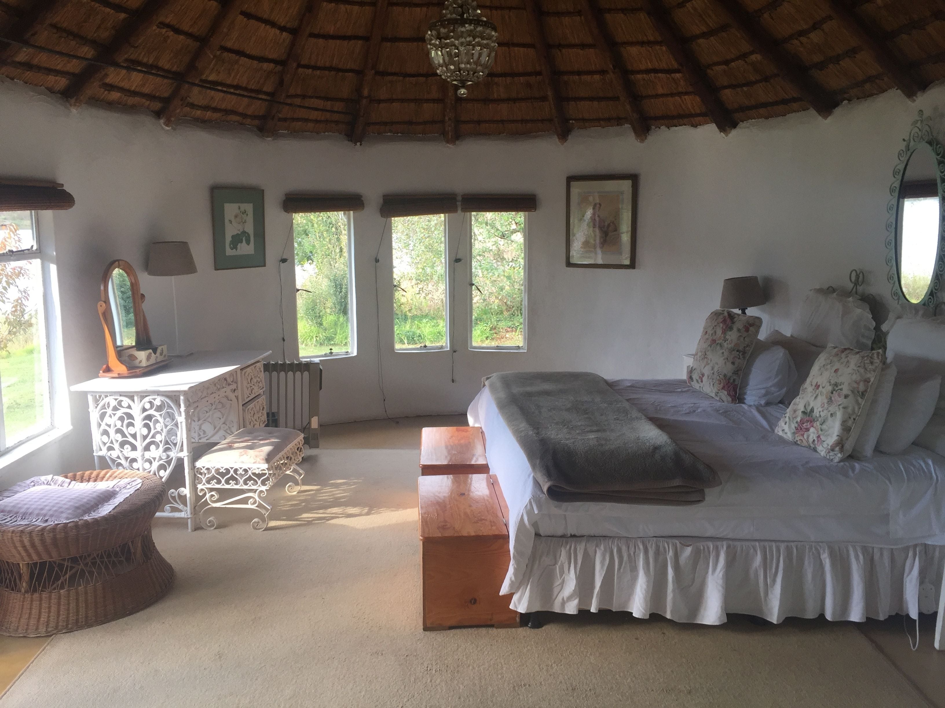 Un dormitorio con cama, cómoda, silla y dos ventanas.