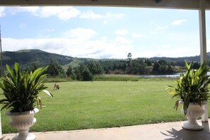 A view from a covered porch with two potted plants, a grassy lawn, and a hilly landscape in the background. - Beacon Vlei Guest Farm (Balgowan)