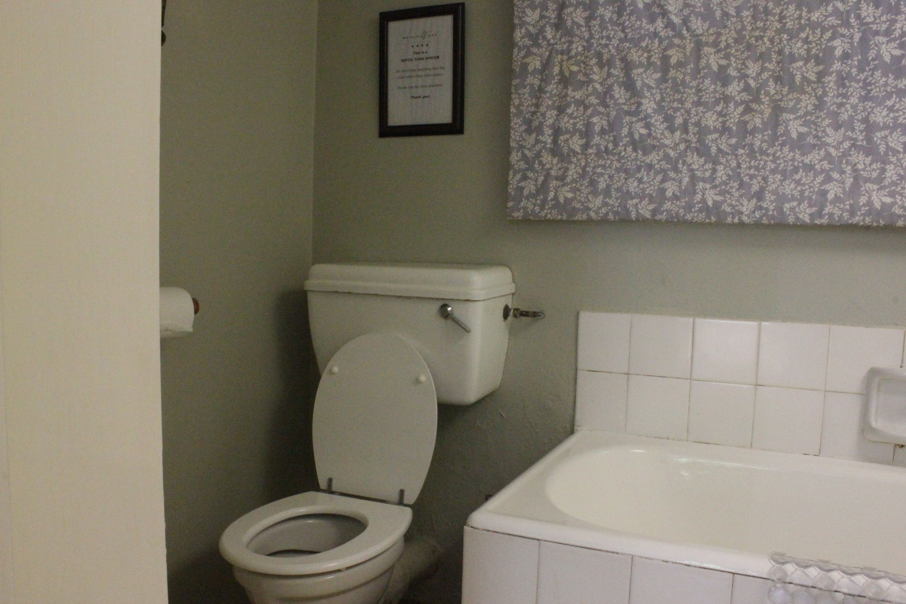 Un baño con inodoro, bañera y un cartel enmarcado en la pared.
