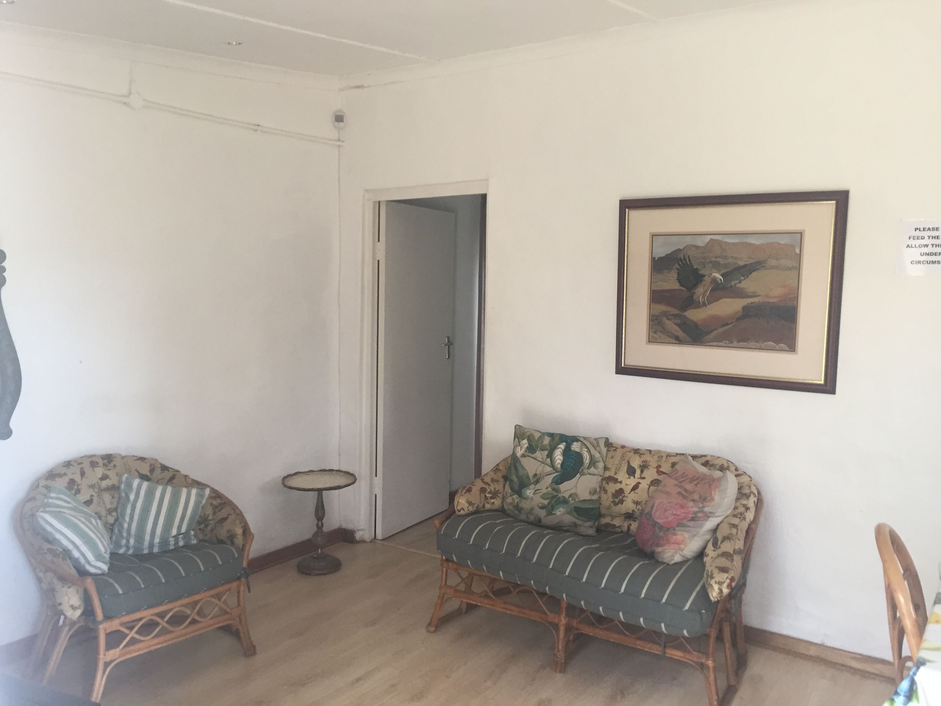 A room with two wicker sofas, one with floral cushions and the other with striped cushions, a small round table, and a framed landscape painting on the wall.