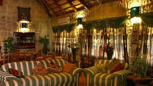 A cozy living room with striped sofas, a fireplace, and draped curtains. - La Rochelle Inn (Richards Bay)