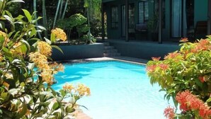 A swimming pool surrounded by lush greenery and a building with large windows. - La Rochelle Inn (Richards Bay)