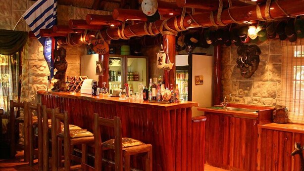 A bar area with wooden furniture, a stone wall, and a thatched roof. - La Rochelle Inn (Richards Bay)