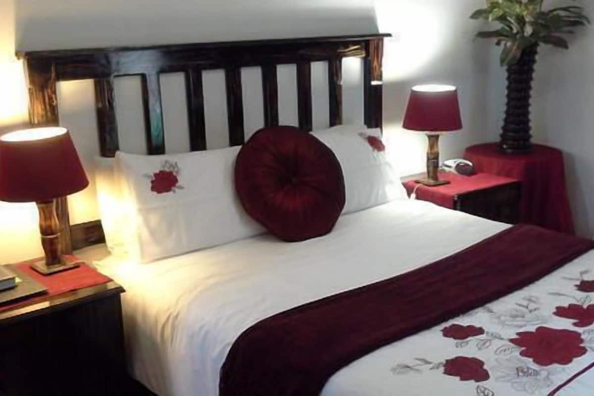 A neatly made bed with a red headboard, two bedside lamps, and a floral-patterned bedspread.