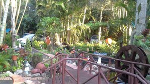 A rustic bridge over a small stream with a water wheel and various garden sculptures. - La Rochelle Inn (Richards Bay)