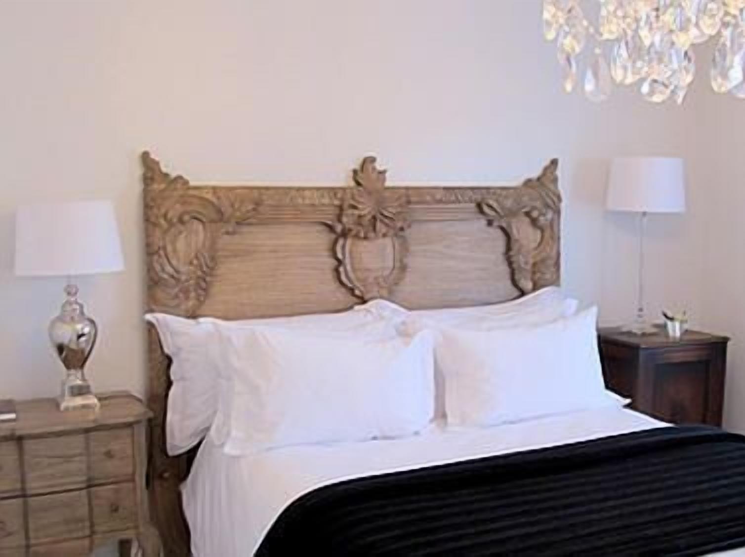 Ein Schlafzimmer mit einem hölzernen Kopfteil, zwei Nachttischen, einer Chandelüster und einem Bett mit weißer Bettwäsche.