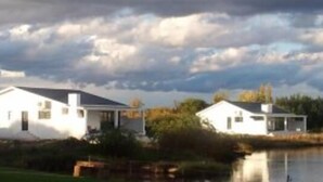 A white house with a porch, situated next to a body of water. - La Riviera Guesthouse (Mohokare)