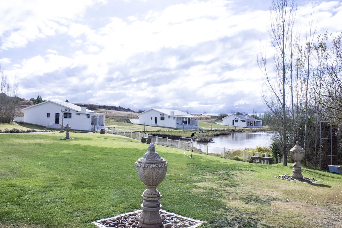 Une propriété paisible au bord d’un lac, avec des maisons blanches, une pelouse bien entretenue et un vase décoratif en premier plan.